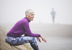 Smiling woman in running gear sits on a foggy beach